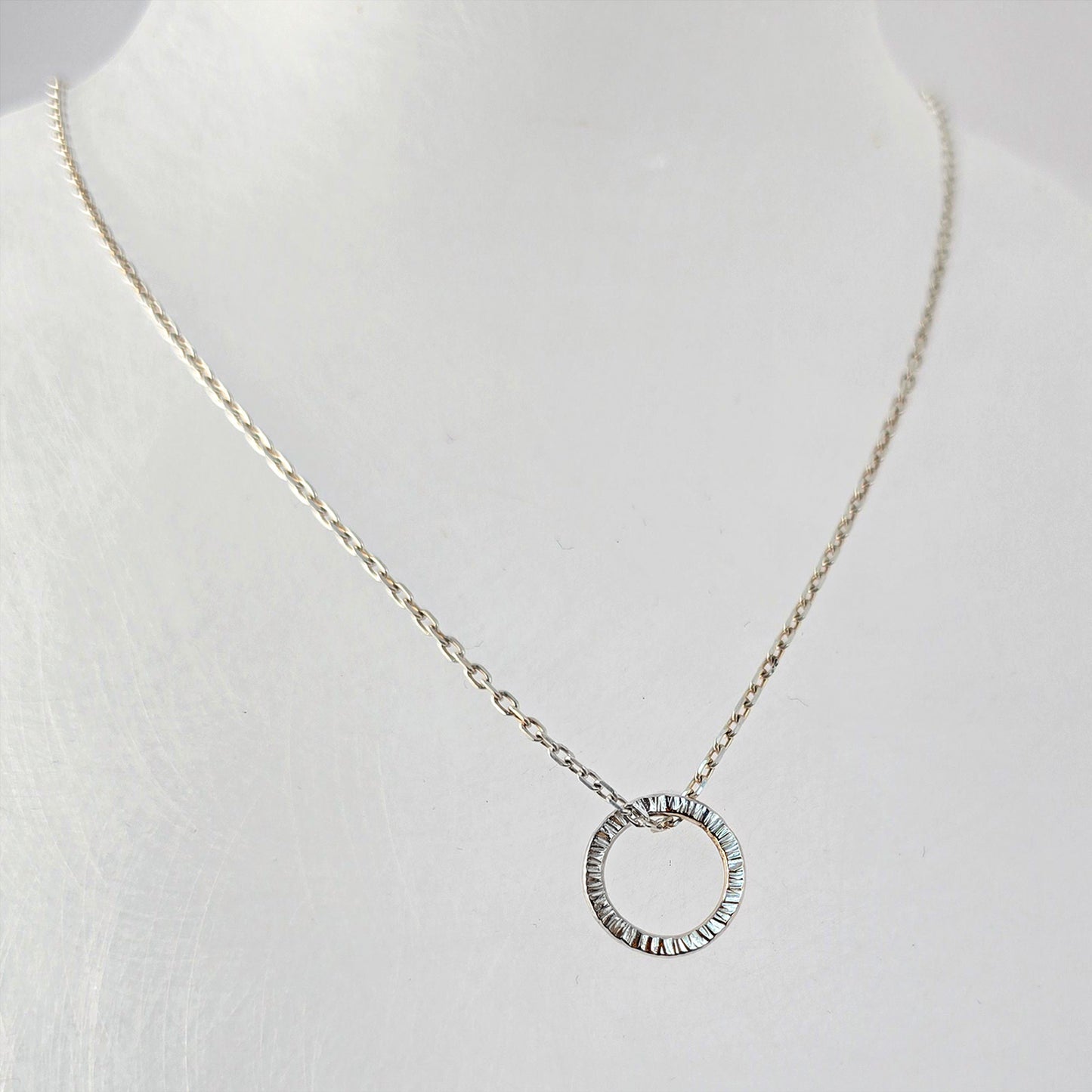 Textured sterling silver circle pendant on a fine silver chain, photographed on a white background.