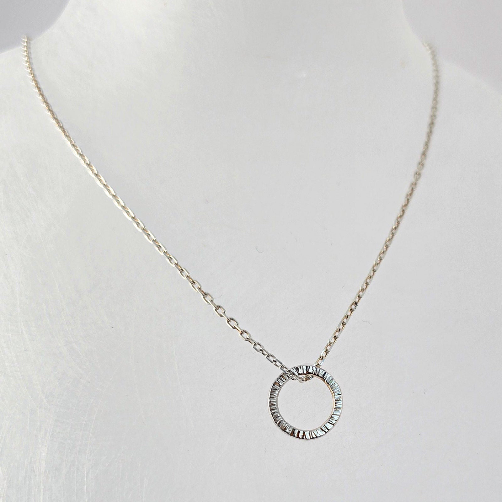 Textured sterling silver circle pendant on a fine silver chain, photographed on a white background.