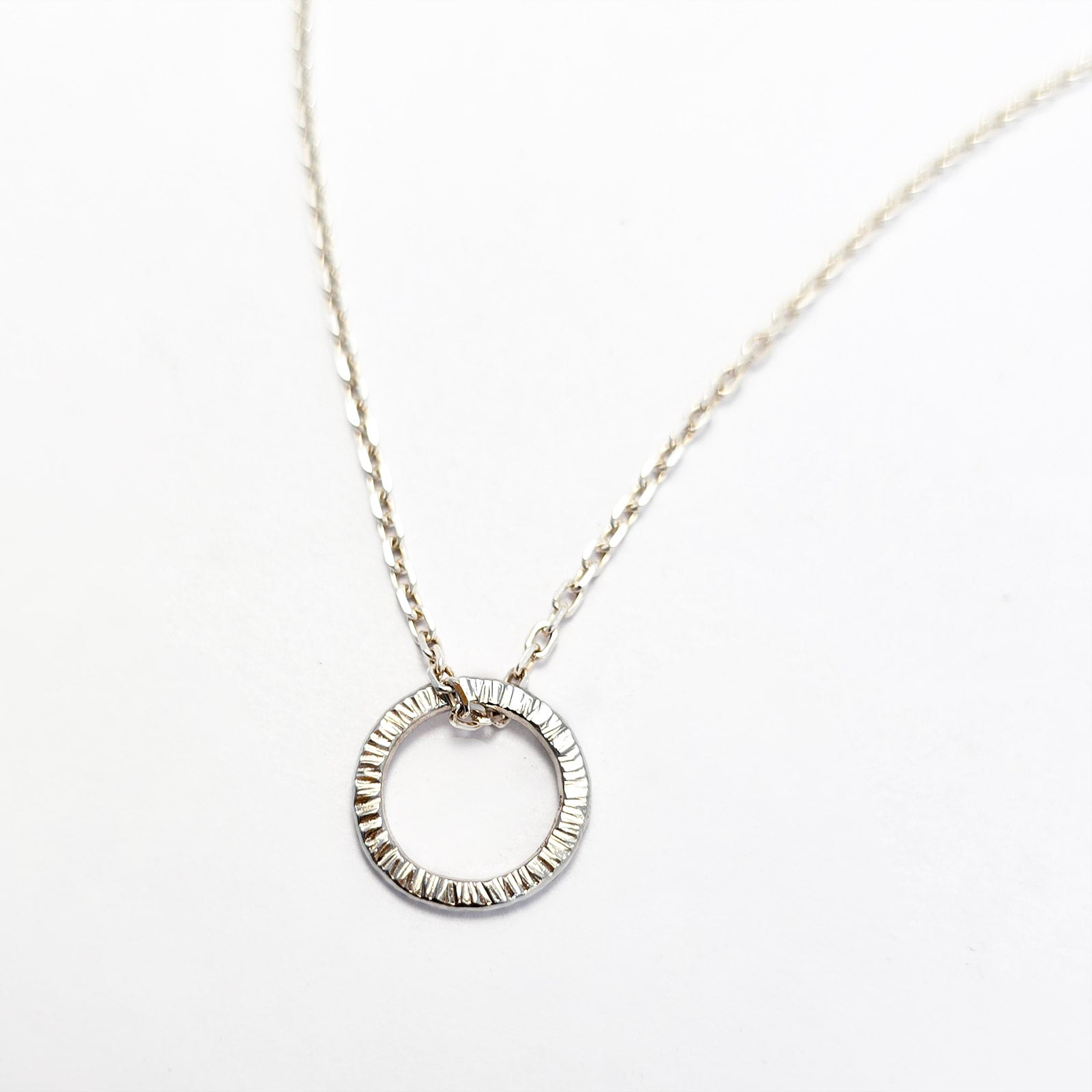 Handmade sterling silver circle pendant necklace with a textured surface, shown on a fine silver chain.