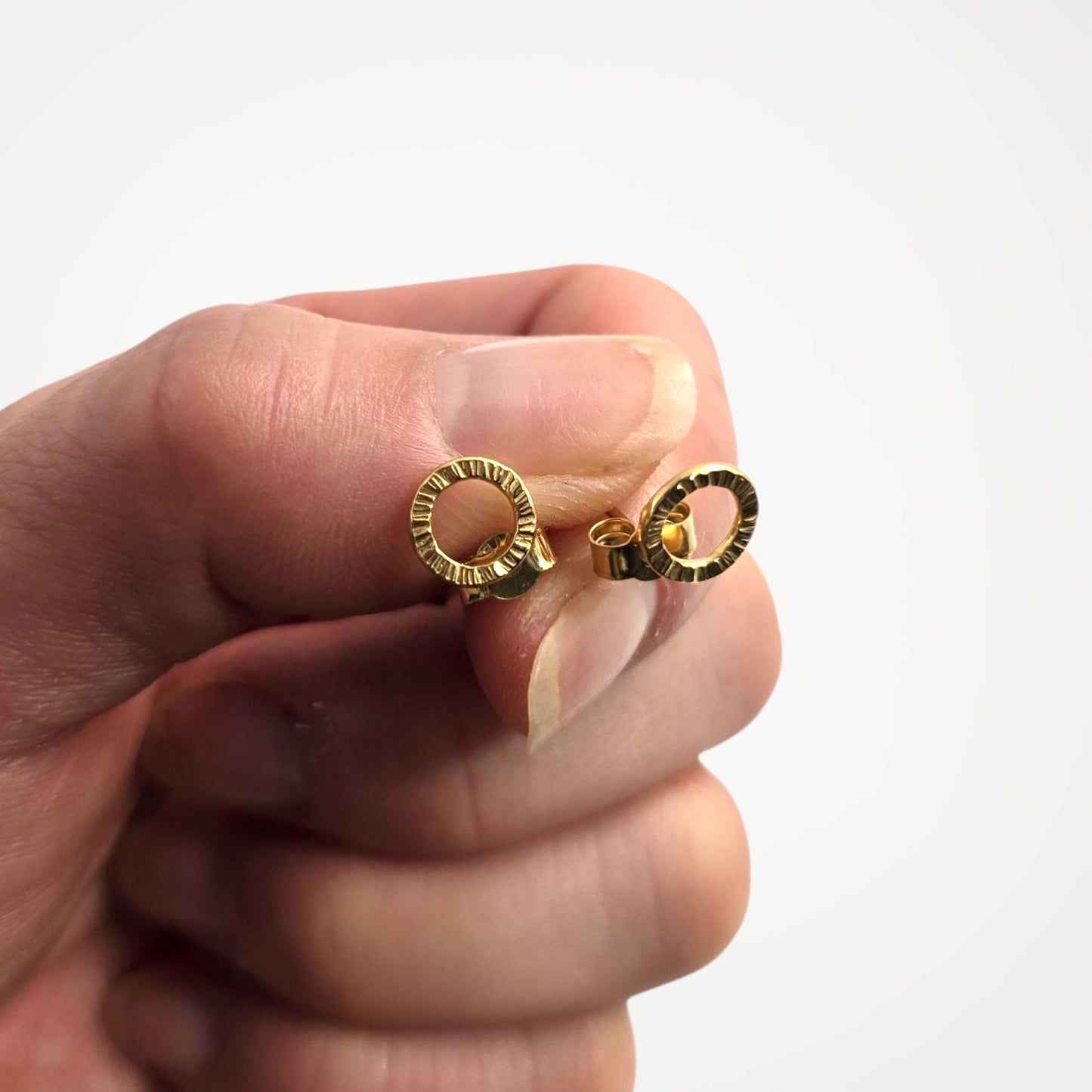 Gold vermeil stud earrings held between fingers against a white background