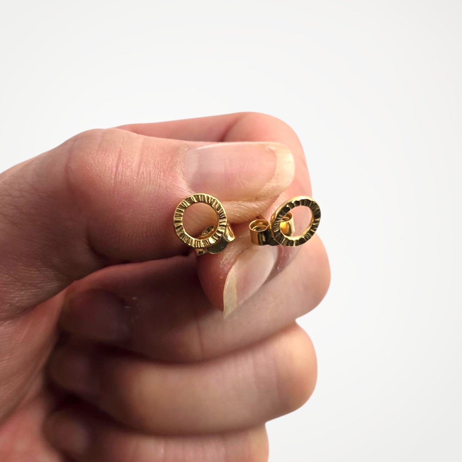 Gold vermeil stud earrings held between fingers against a white background