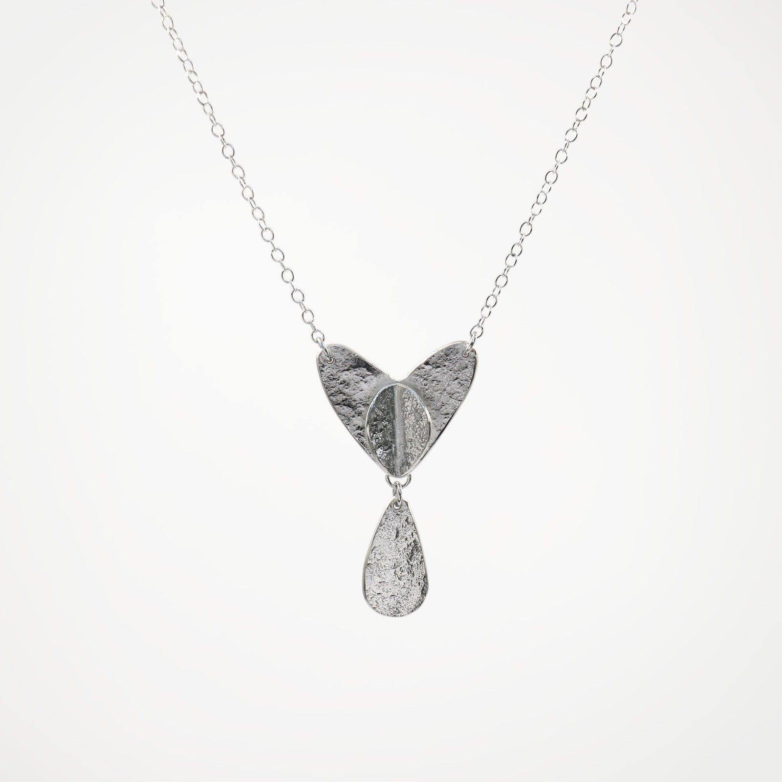 Silver necklace with a heart-shaped pendant and teardrop charm on a white background