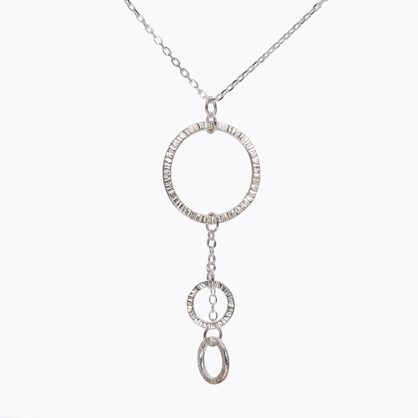 A silver necklace with a central circular pendant and two smaller textured circles, suspended from a larger circle.