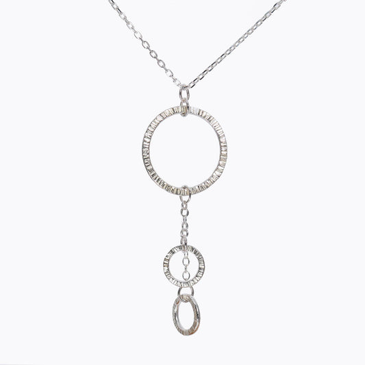 A silver necklace with a central circular pendant and two smaller textured circles, suspended from a larger circle.