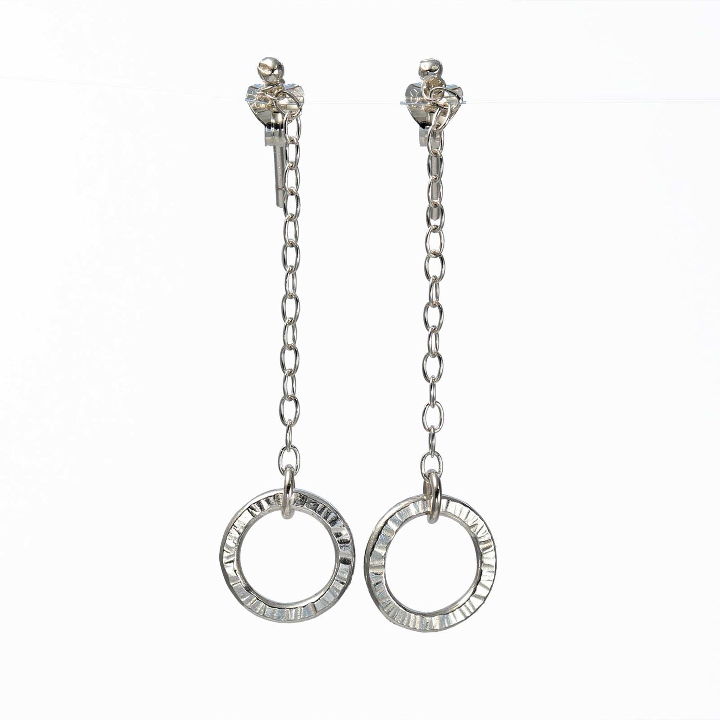A pair of silver hoop earrings with intricate detailing, suspended on a delicate chain.
