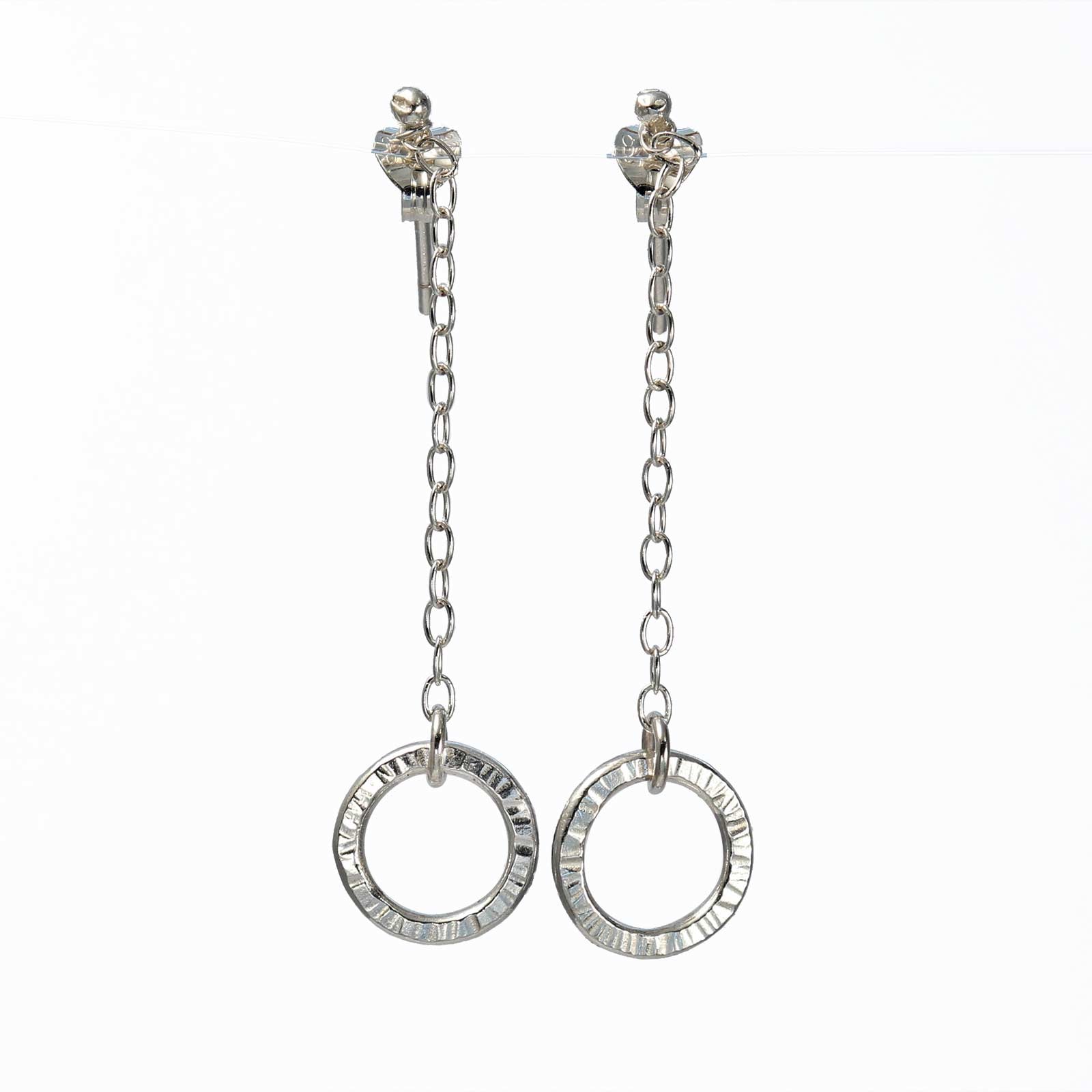 A pair of silver hoop earrings with intricate detailing, suspended on a delicate chain.